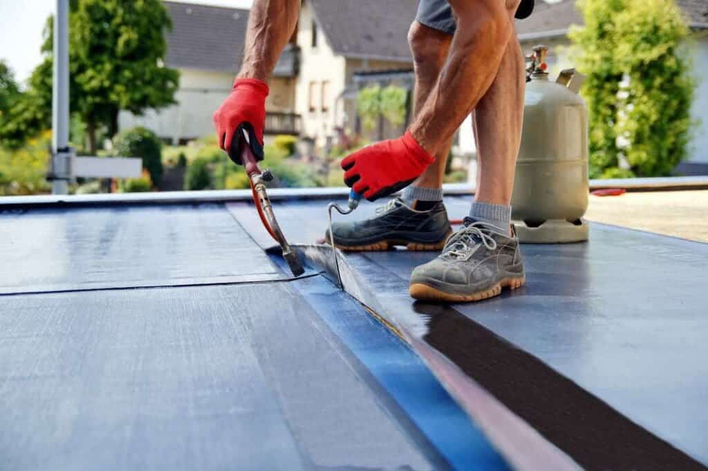 A bottom view of a person using a tool to lay roll roofing