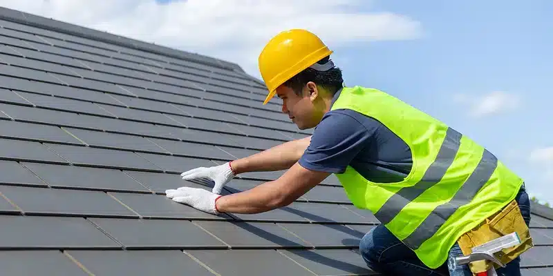 A view of a contractor wearing a hat inspecting a roof