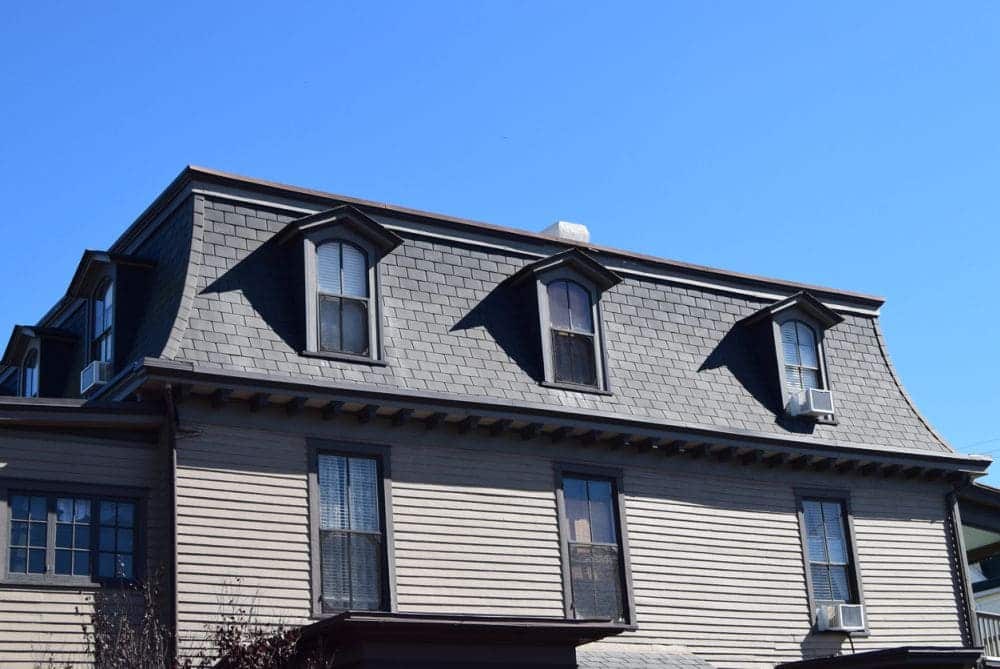 A view of a grey mansard roof house with windows