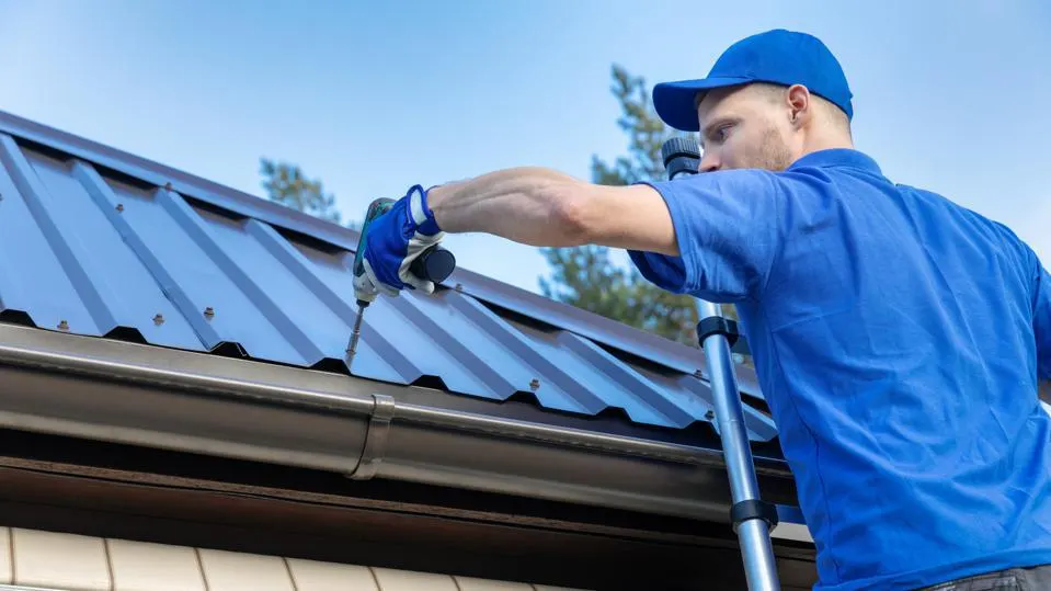 A view of a person in blue drilling inside a metal roof