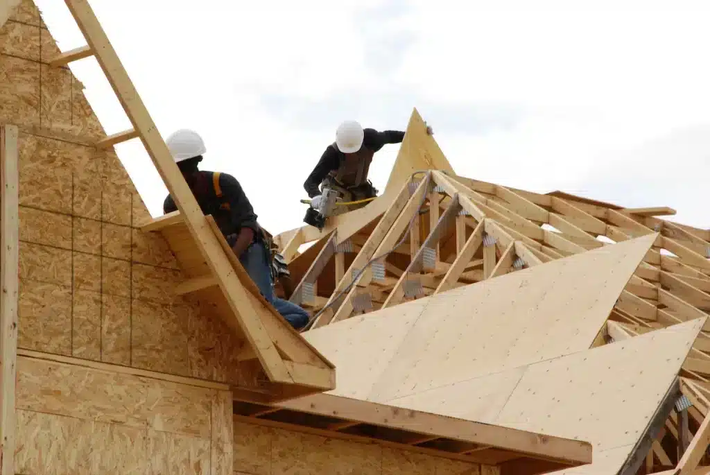 A view of contractors placing a plywood sheathing over a house roof during construction