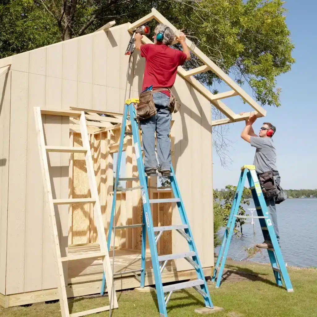 persons building a shed roof standing on ladders