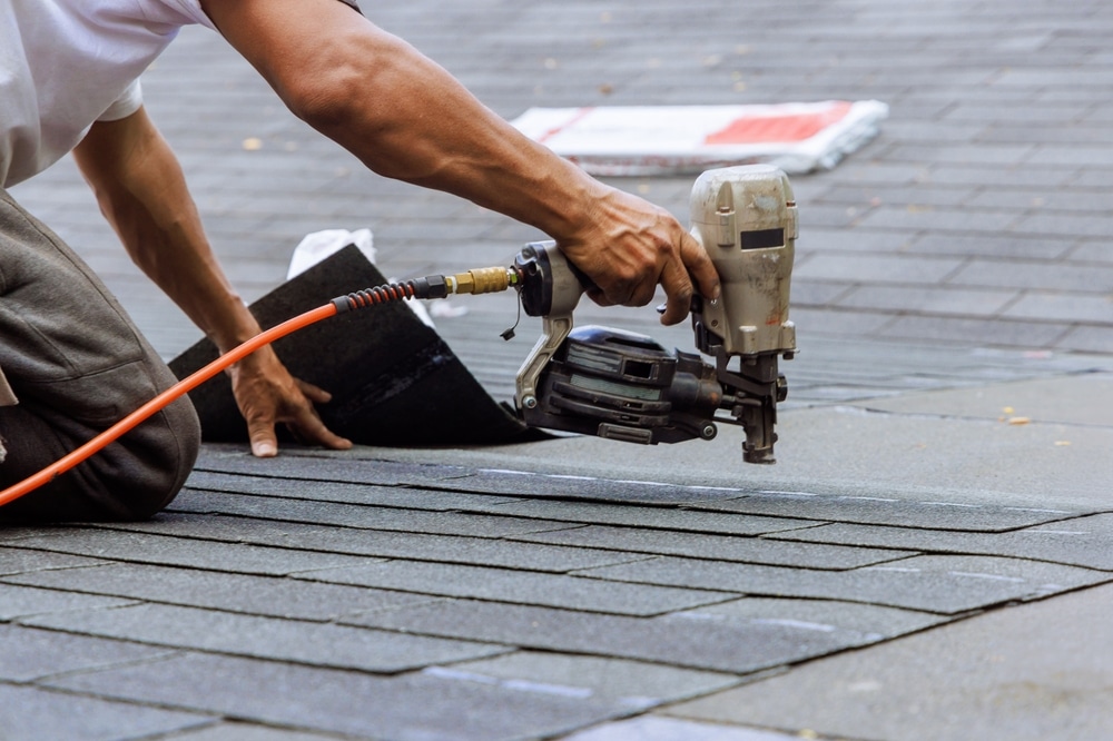 Air pneumatic nail gun used by roofer to install new asphalt bitumen shingles