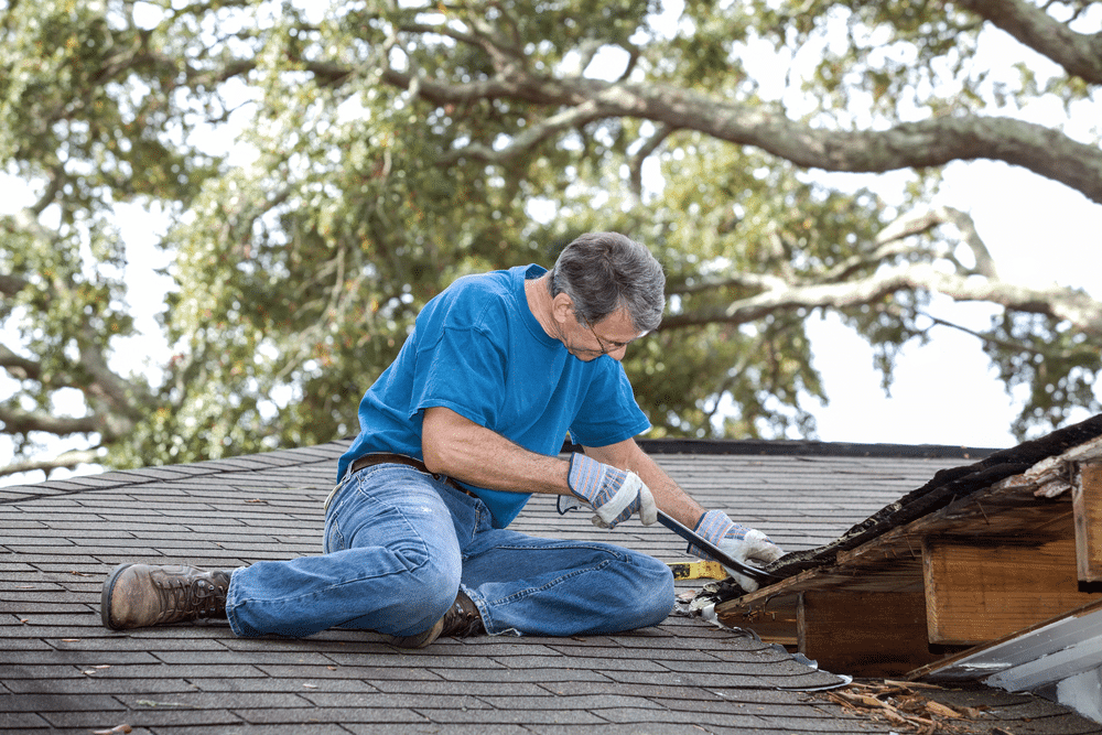 Man using crowbar to remove rotten wood from leaky roof