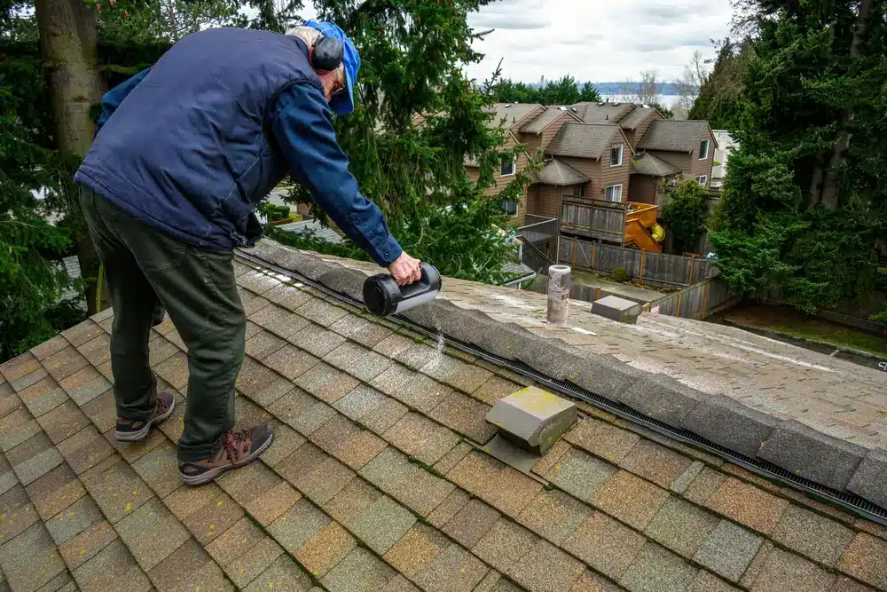 Senior man with a container of moss killer spreading the granules on a residential asphalt shake roof