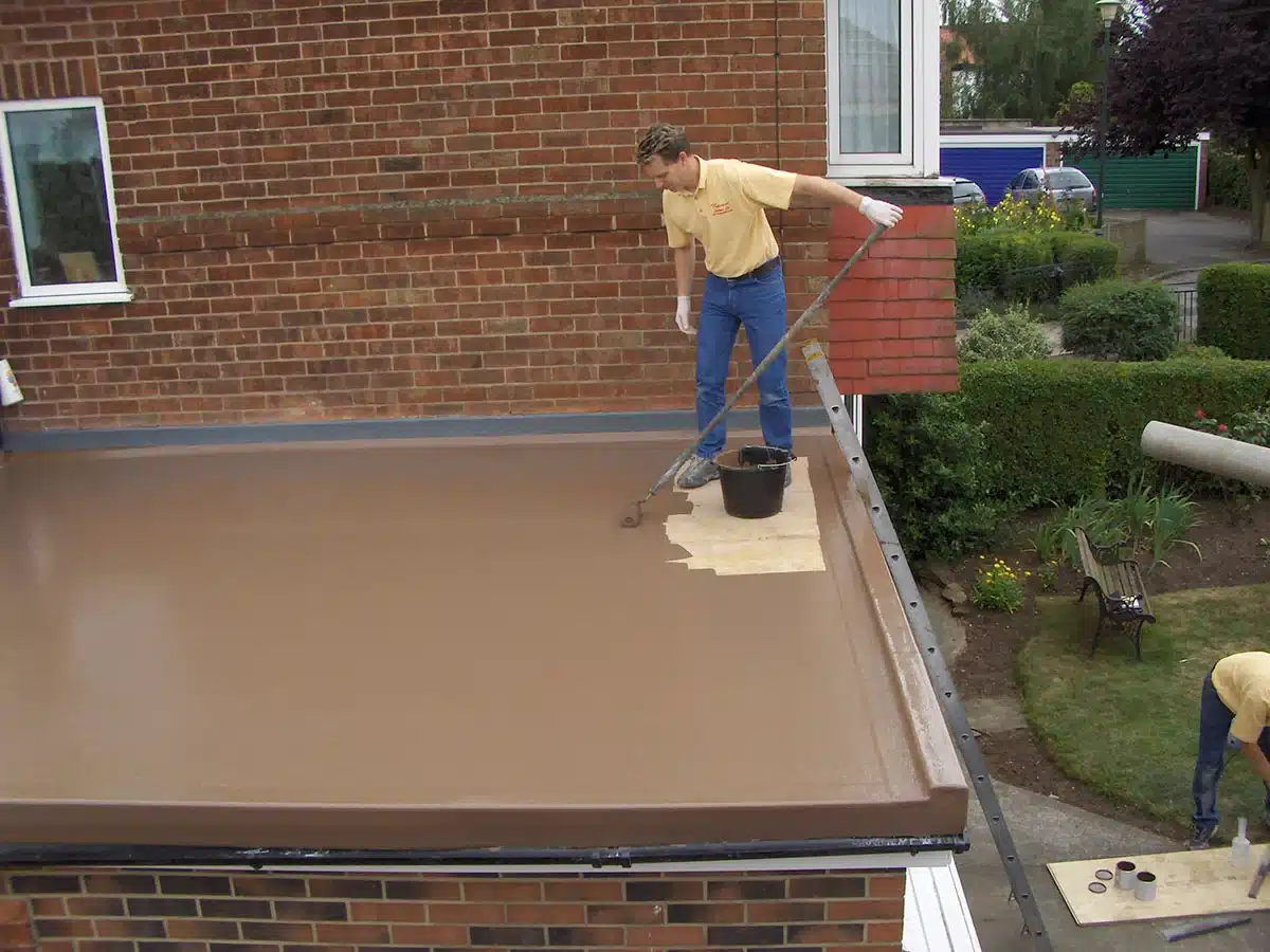 a roofer applying fibreglass roofing layer on a roof a roofer applying fibreglass roofing layer on a roof