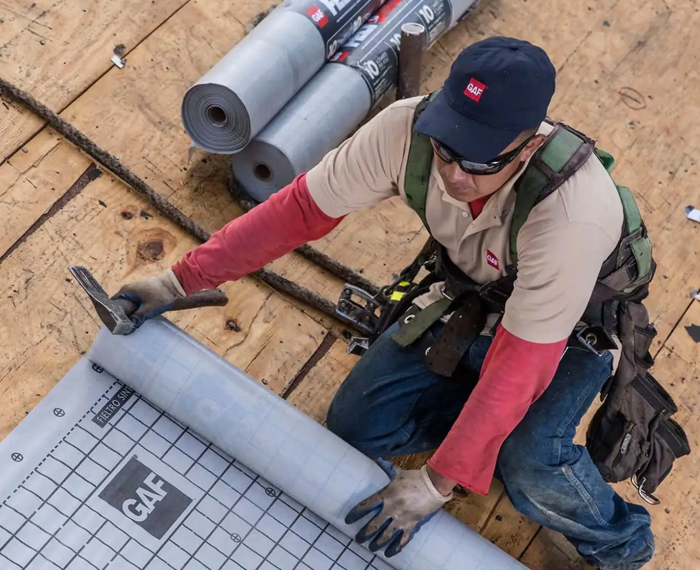 view of a person unfolding a roof underlayment sheet and holding a hammer view of a person unfolding a roof underlayment sheet and holding a hammer
