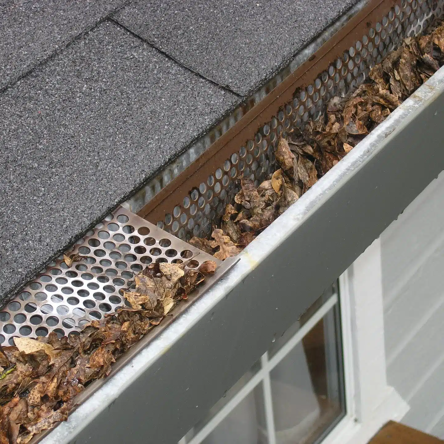 Clogged gutter with leaves and debris which can cause water backup and potential roof damage