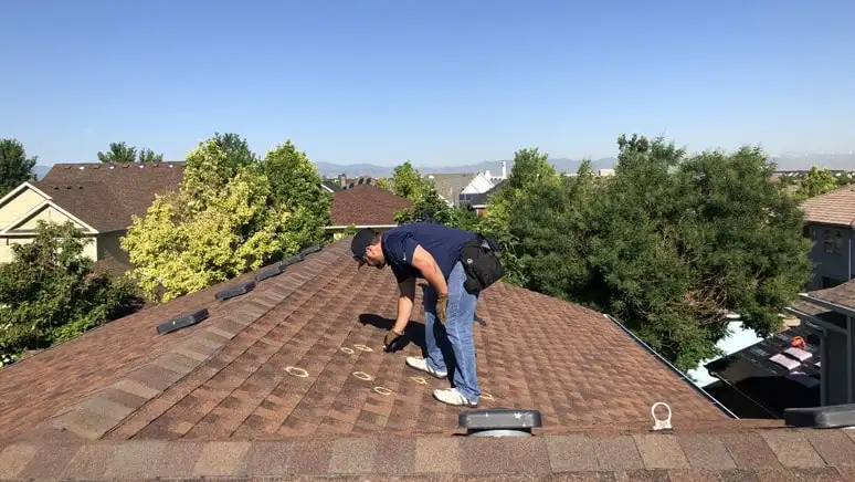 Roof inspector marking areas of concern on asphalt shingles during a roof inspection