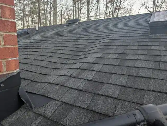 Wavy or buckled asphalt shingles possibly due to moisture damage or improper installation